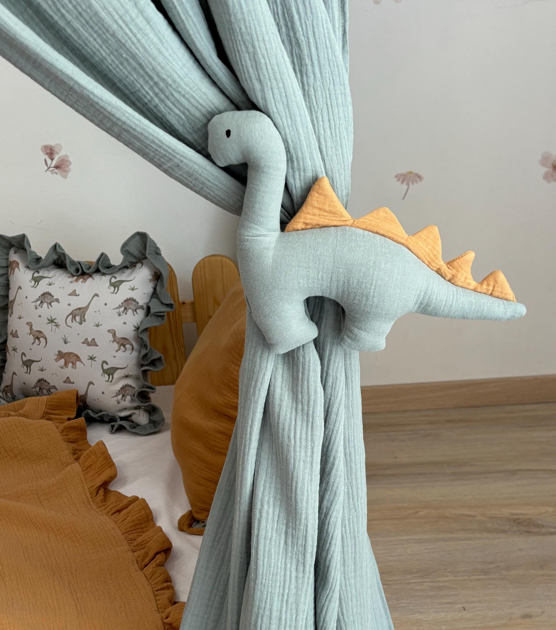 Sage green canopy with dinosaur tiebacks over Montessori bed
