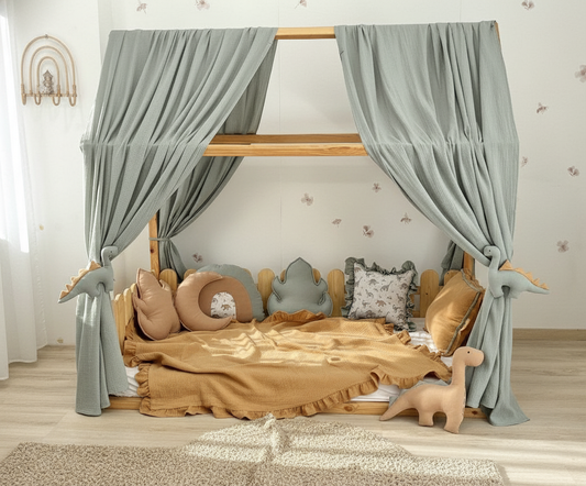 Sage green canopy with dinosaur tiebacks over Montessori bed
