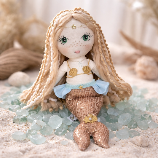 Handmade mermaid doll with hand-stitched face, yarn hair and soft fabric tail, styled in a neutral beach-inspired setting