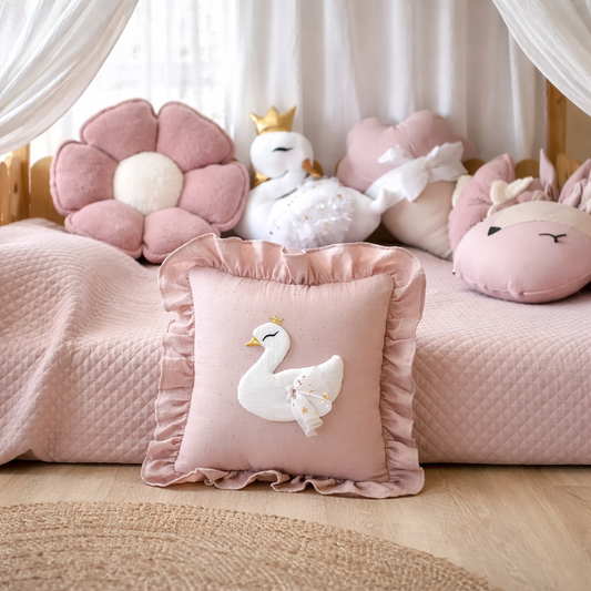 Pink pillow with a swan design on a bed with other decorative pillows.