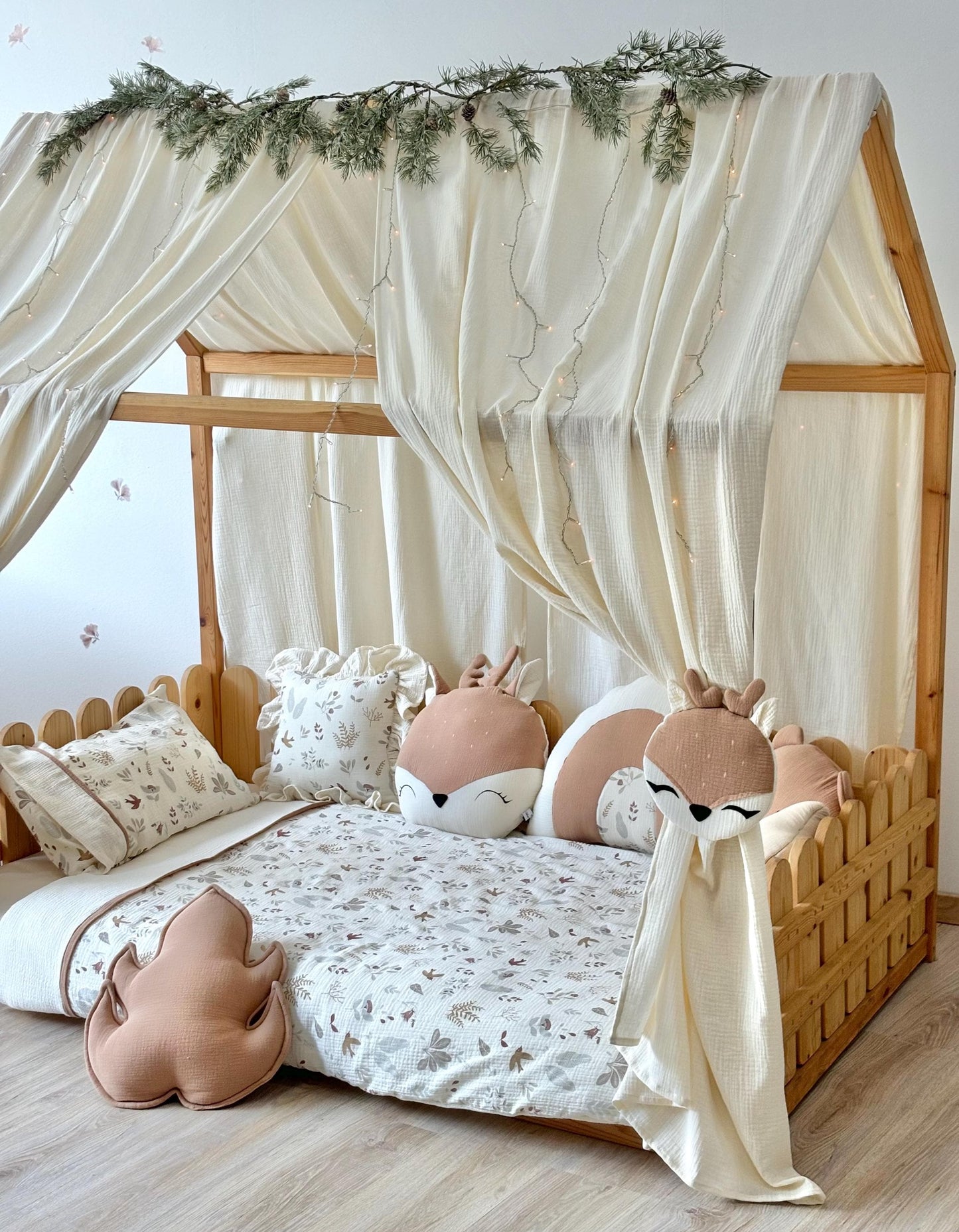 Neutral playroom setup with muslin canopy, wooden bed frame and cuddly stuffed animals.
